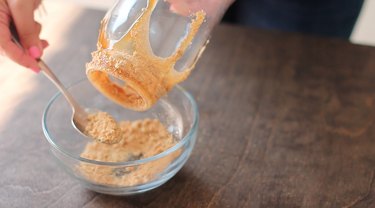 Sprinkling graham cracker crumbs onto drips of caramel sauce on jar.